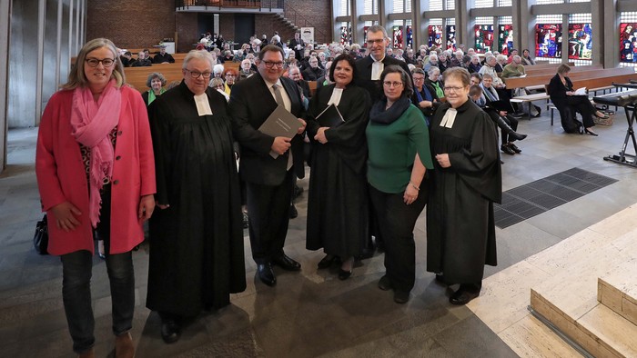 Ein Gruppe von Menschen posiert in einem großen, hellen Raum mit hohen Fenstern und einer Orgel.
