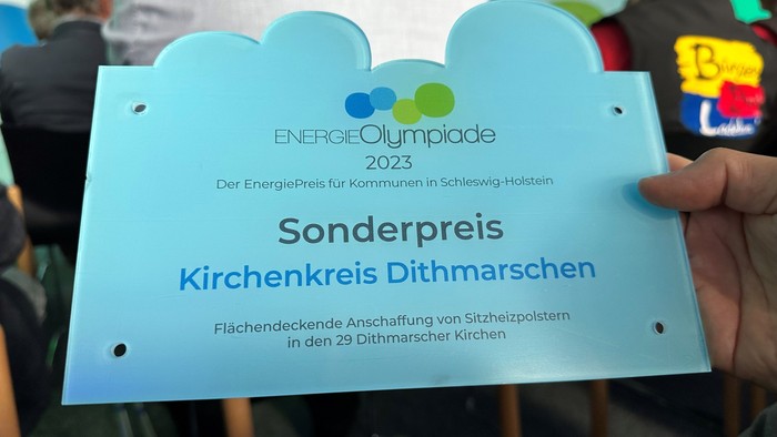 Person hält Preisplakette der EnergieOlympiade 2023 für Kirchenkreis Dithmarschen