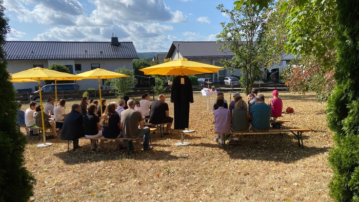 Eine Gruppe von Menschen sitzt an Tischen unter gelben Sonnenschirmen im Freien.
