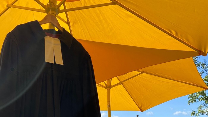 Ein schwarzer Talar hängt an einem gelben Sonnenschirm im Freien