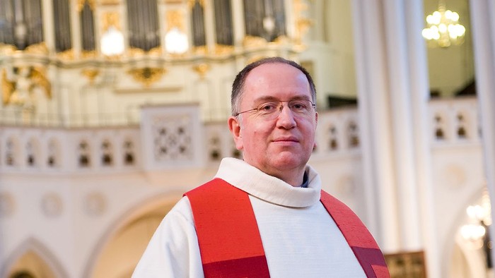 Ein Mann in kirchlicher Kleidung vor einem Kircheninneren.