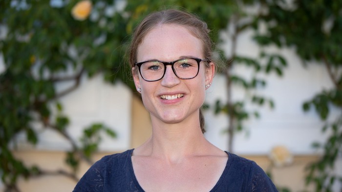 Junges Mädchen mit Brille und blauer Bluse lächelt.