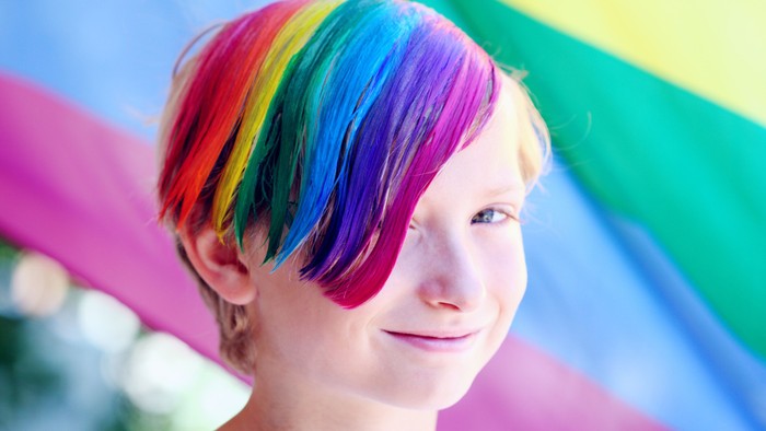 Ein Kind mit bunt gefärbten Haaren vor einem Regenbogenfahne