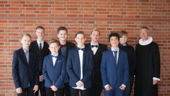 En gruppe drenge i formelle klæder står foran røde mursten.
