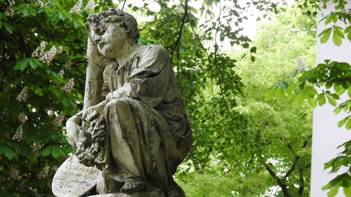 Die Statue einer Frau sitzt unter grünen Bäumen.