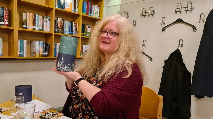 Frau mit langen blonden Haaren hält eine Tasse in einem Café