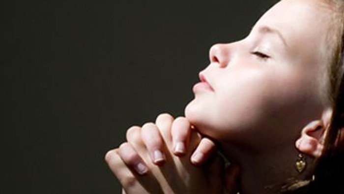 Ein Mädchen betet mit gefalteten Händen.