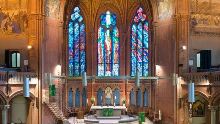 Innenraum einer Kirche mit bunten Glasfenstern und hohem Altar