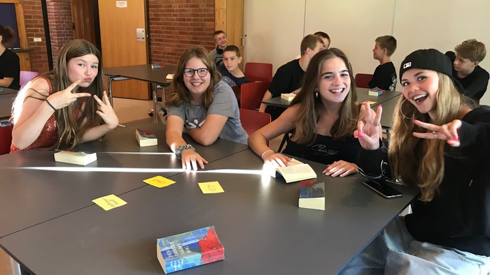 En gruppe unge kvinder sidder ved et bord i en biblioteksafdeling og ser glade ud.