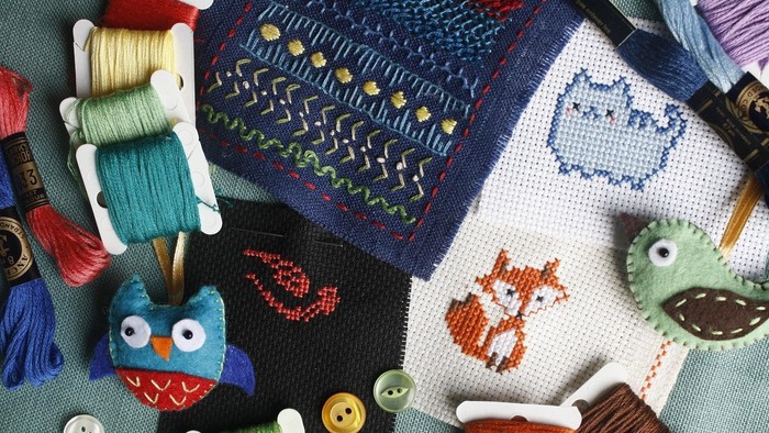 Das Bild zeigt verschiedene Näh- und Stickutensilien, darunter Garnspulen, Knöpfe und Stickereien.