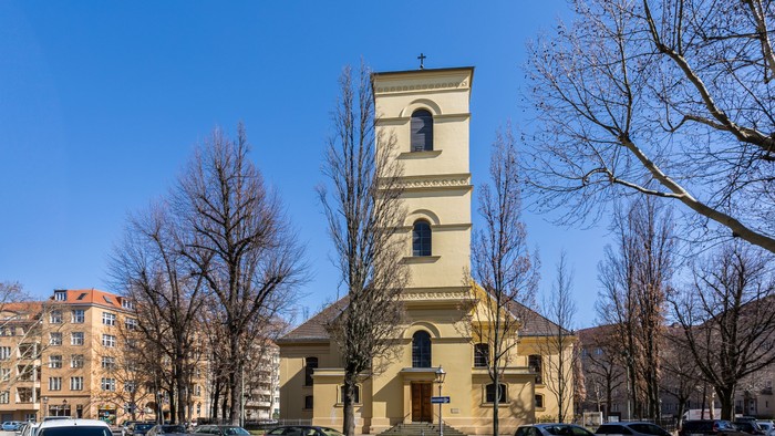 Gelbe Kirche mit hohem Turm und Parkplatz davor