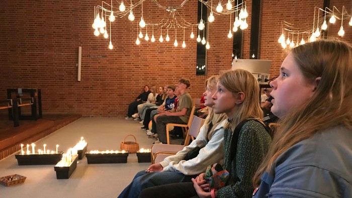 En gruppe unge sidder i en rummelig lokal med hængende lys og lysende lygter på gulvet.