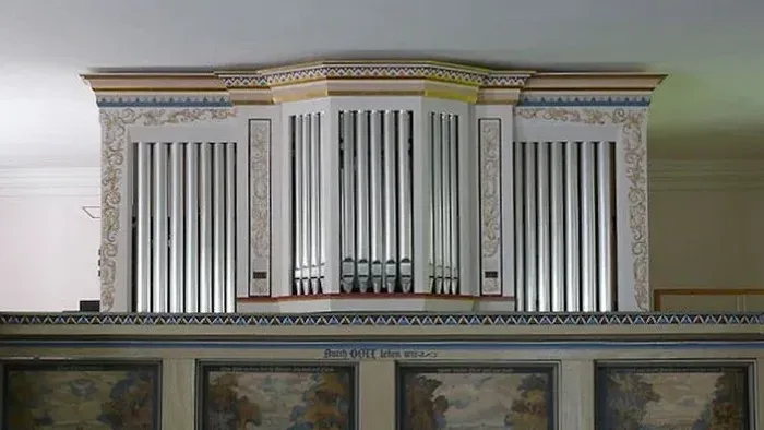 Das Bild zeigt eine verzierte Orgel mit vier Bildern darunter.