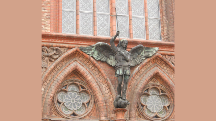 Die Statue eines geflügelten Engels vor einem Ziegelgebäude mit Buntglasfenstern.