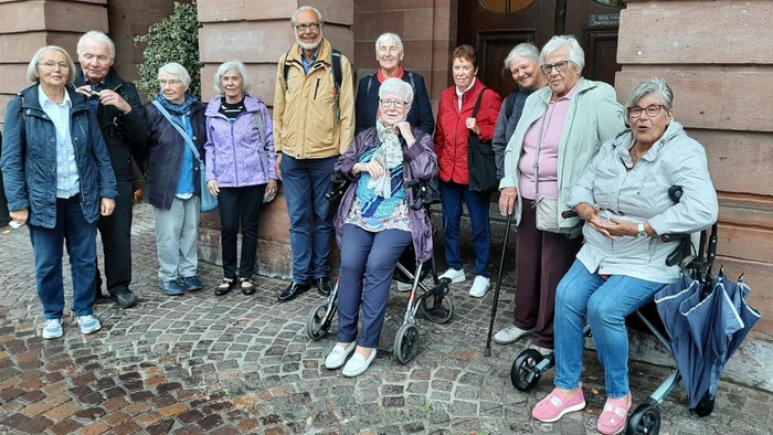 Eine Gruppe älterer Menschen steht vor einem Gebäude, einige mit Gehhilfen.