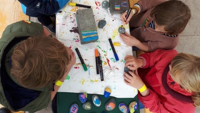 Kinder sitzen um einen Tisch und malen mit Buntstiften und Wasserfarben.