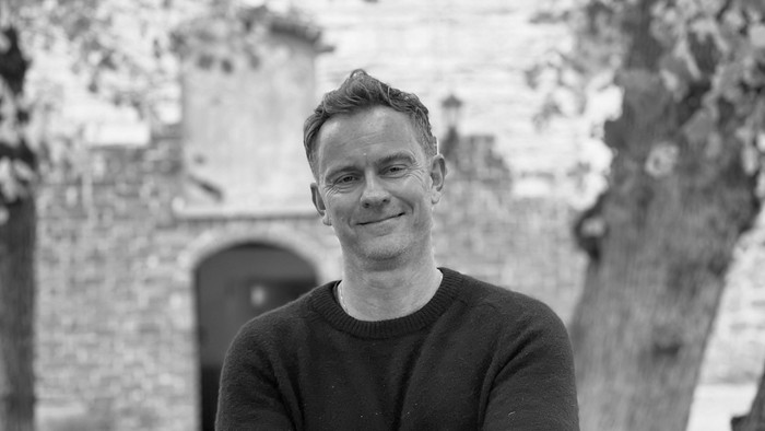 Mand står i forgrunden med træ i baggrunden