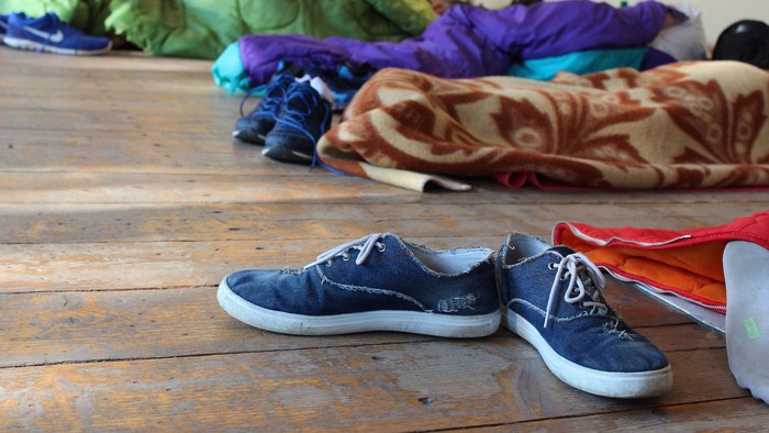 Auf dem Holzboden stehen zwei blaue Turnschuhe neben einem Haufen farbiger Kleidung.