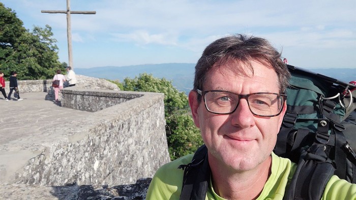 Mann mit Rucksack vor Kreuz und Bergblick