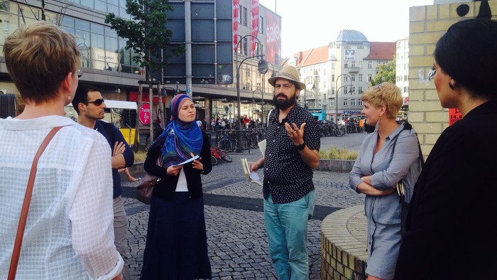 Eine Gruppe von Menschen steht auf einem Kopfsteinpflasterplatz und unterhält sich.