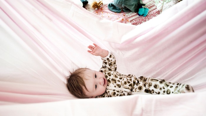 En baby rækker ud under bløde, draperede tæpper i en hyggelig, legesyg stemning.