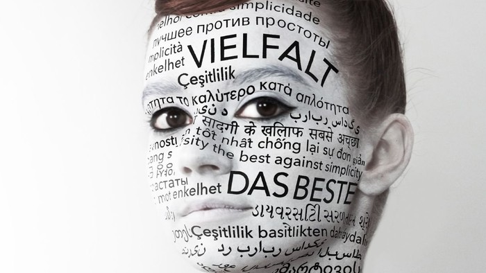Das Bild zeigt eine Frau mit Texten in verschiedenen Sprachen auf ihrem Gesicht.
