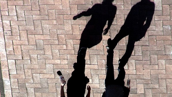 Drei Personen werfen Schatten auf einem Kopfsteinpflaster.