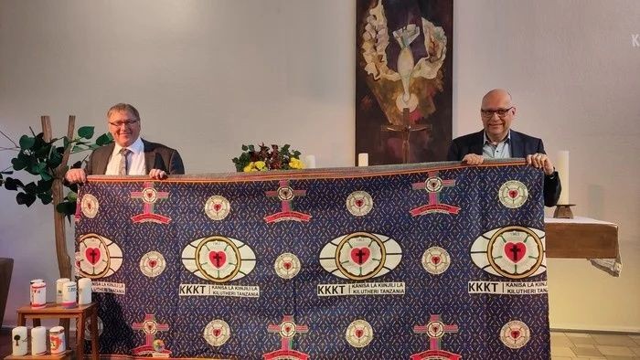 Zwei Männer hinter einem Podium mit Herzmotiven, einer spricht in ein Mikrofon