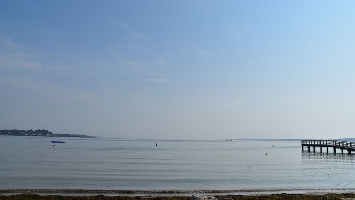 Ein ruhiger Strand mit einem Pier, der ins Meer ragt, unter einem klaren blauen Himmel.