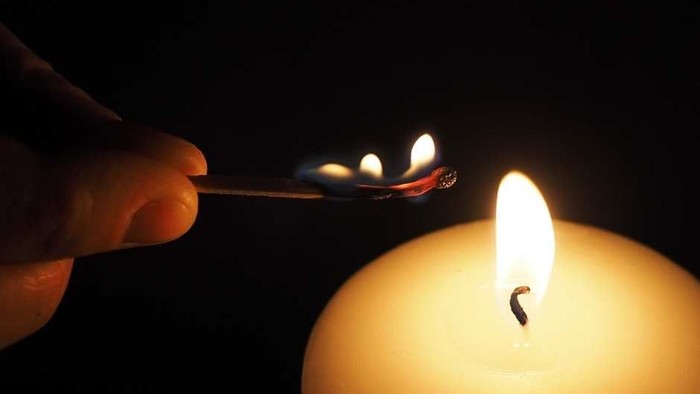 Eine Hand hält ein Feuerzeug vor einer brennenden Kerze