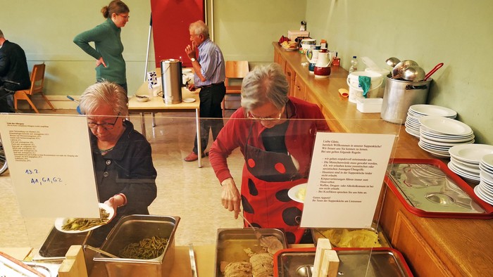 Ein Buffet mit verschiedenen Gerichten, mehrere Menschen bedienen sich.
