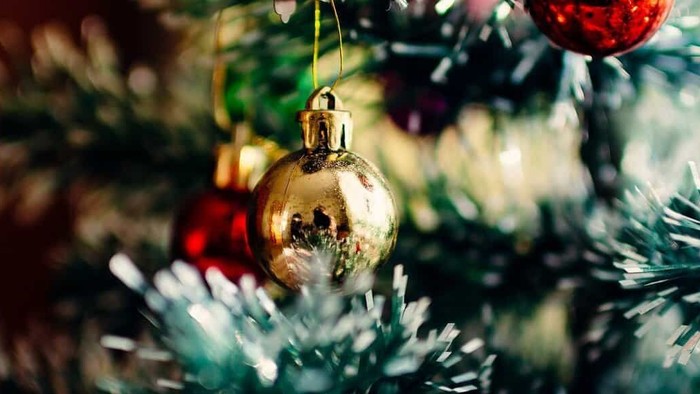 En juledekoreret træ med guldfarvede glaskugle og røde pynt.