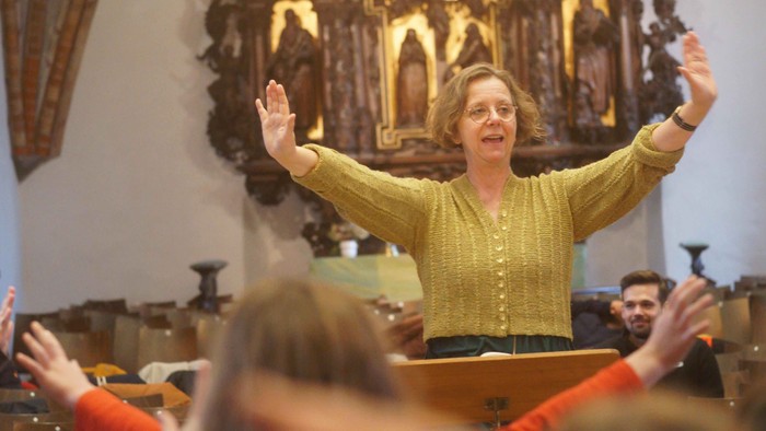 Eine Frau steht mit erhobenen Armen in einer Kirche und leitet eine Gruppe an.