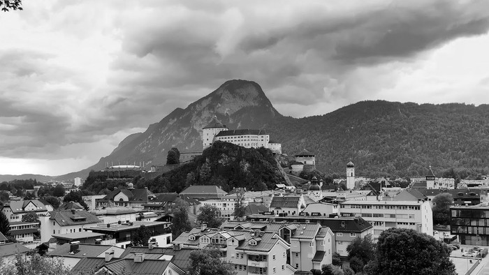 Städtische Landschaft mit Burg auf hohem Felsen, umgeben von Bergen und Wolkenhimmel