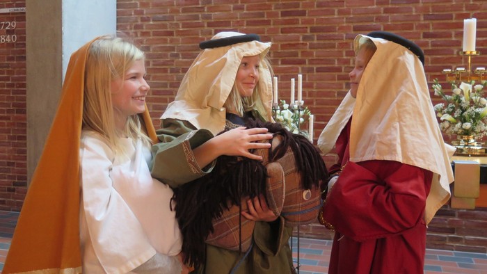 Tre piger i kostumer og hårdeker i kirke