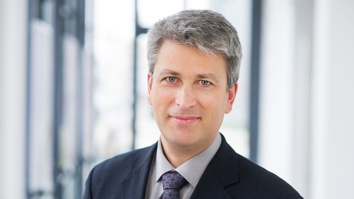 Ein Mann in Anzug und Krawatte steht vor einem Fenster.