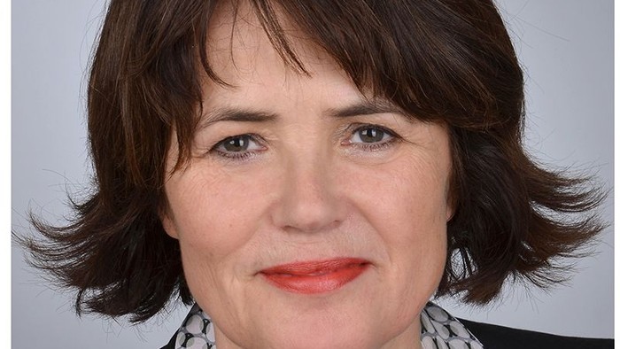 Eine Frau mit kurzem braunen Haar und rotem Lippenstift lächelt in die Kamera.