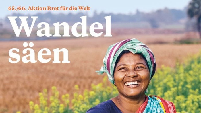 Eine lächelnde Frau in farbenfroher Kleidung steht inmitten eines üppigen grünen Feldes und wirbt für nachhaltige Landwirtschaft.