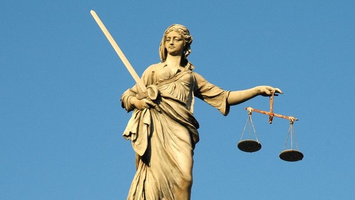 Die Statue einer Frau mit Schwert und Waage vor blauem Himmel