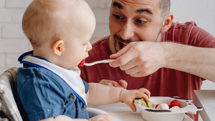 Vater füttert Baby am Hochstuhl mit Löffel