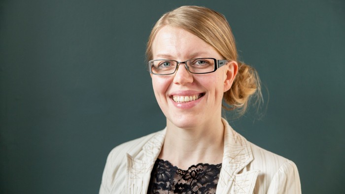En kvinde med blondt hår og briller smiler til kameraet.