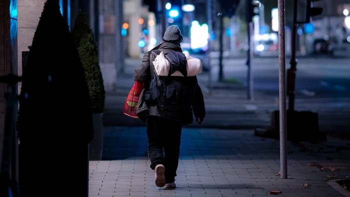 Person geht nachts mit Rucksack und Einkaufstüte durch die Stadt