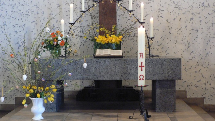 Ein Altar in einer Kirche mit Kerzen, Blumen und einem Kater davor