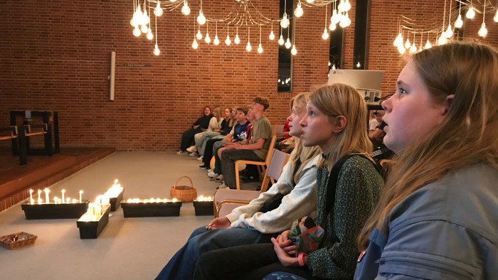 En gruppe unge sidder i en rummelig lokal med hængende lys og lysende lygter på gulvet.