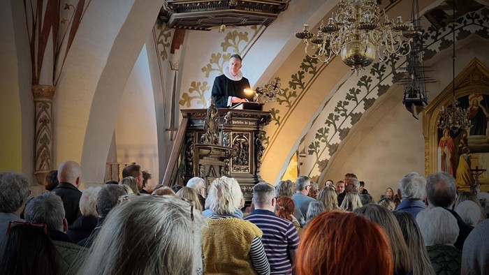 En præst holder en prædiken fra en pulpet i en kirke med en tilstedeværende menighed.