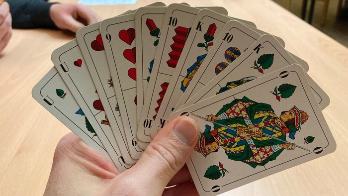 Eine Hand hält einen Fächer aus Spielkarten auf einem Tisch