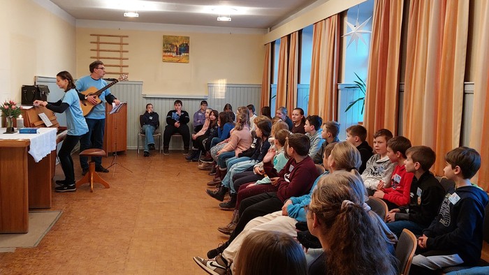 Eine Gruppe von Menschen hört einem Mann mit Gitarre zu.