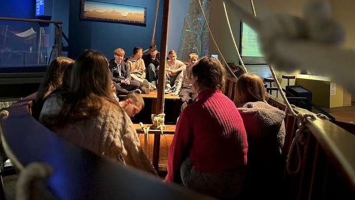 Menschen sitzen in einem Boot und hören einem Mann zu.