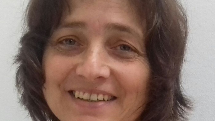 Eine Frau mit dunklem, kurzen Haar und einem gestreiften Hemd lächelt.