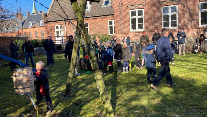 En gruppe af mennesker samles på en græsplæne foran et rødt teglstenhus, hvor en person tager et billede af en stor, grøn skørtelstand.